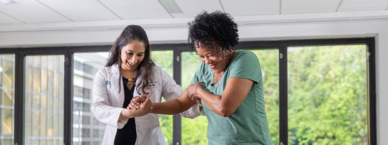 Doctor assisting a patient with physical therapy, helping her move her arm.