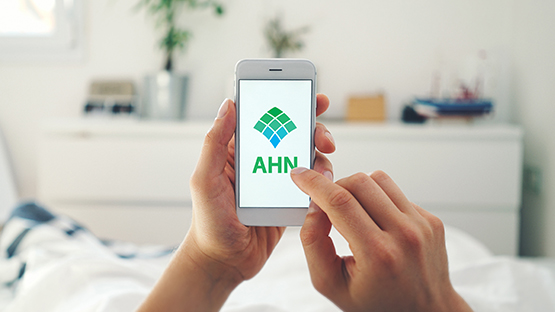 A person's hands holding a phone displaying AHN's website.