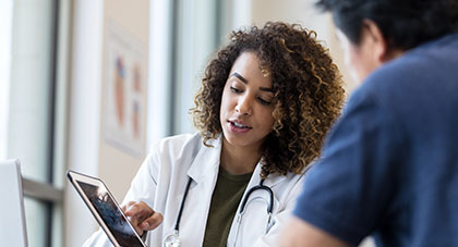 A doctor consulting with a patient over their x-ray that is displayed on the tablet that she is holding.