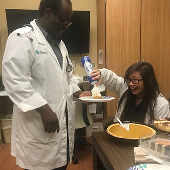 Man standing and holding plate with pie while sitting woman with can of whipped cream puts some on his pie