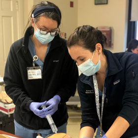 Two residents wearing masks in simulation lab enhancing their skills. 