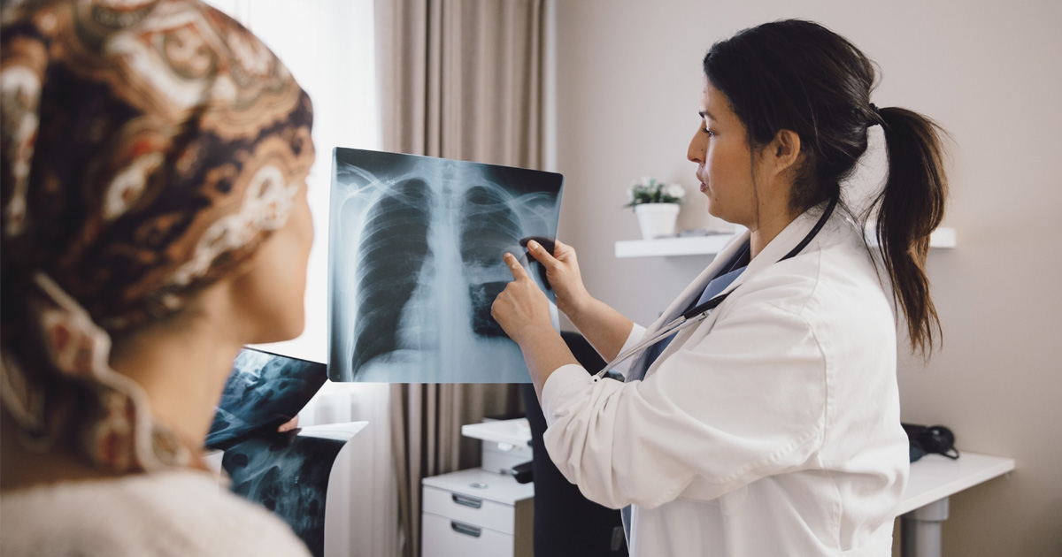 A female medical professional in a white coat shows an X-ray to a patient.
