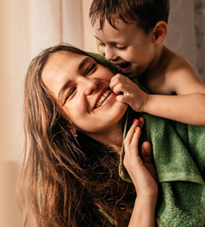 A small boy climbing on his mother's back while she smiles looking back at him