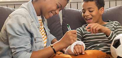 Young girl smiling as she signs her younger brother's cast on his broken arm 