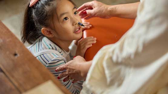 Small girl with a crayon stuck in her nose looking up at her caretaker