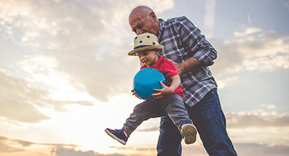 grandfather lifting up his grandson as he plays with a ball