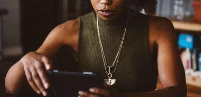 A woman reading news article on tablet at her kitchen table.