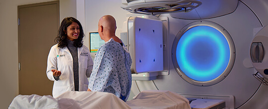 Radiation oncologist with patient next to glowing blue therapy machine.
