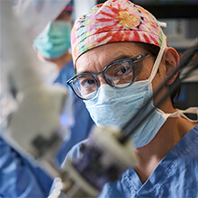 Surgeon in glasses, cap, mask, focused on operation. 