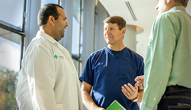  Two medical professionals talk to a patient in a bright hallway.