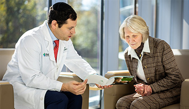 Doctor shows brochure to an older patient in a bright room.