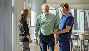 A medical professional in blue scrubs talks with a man and woman.