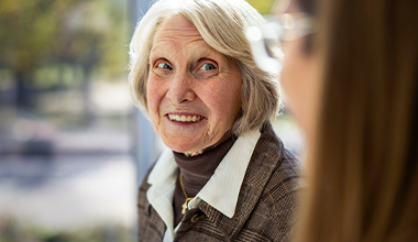 An older white woman with gray hair smiles at someone off-camera.