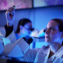 A white medical professional in a white coat talks to a woman with a blurry foreground.