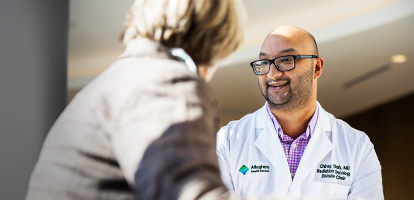 A male South Asian medical professional in a white coat smiles while looking at a woman.