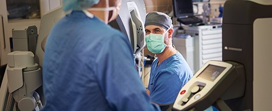 A white medical professional in a lab coat looks at a slide in a blue-lit room.