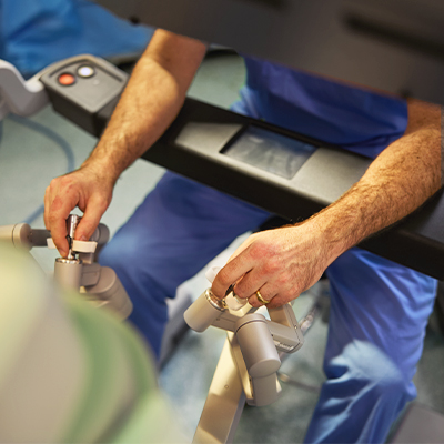 A medical professional in a surgical cap and mask operates a robot in an operating room.