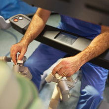 A medical professional in a surgical cap and mask operates a robot in an operating room.