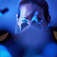 A medical professional in blue scrubs holds a folder and talks to a man and a woman.