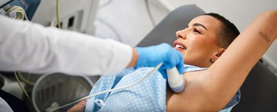 Female patient in a gown with a medical instrument being held to her upper torso by a gloved hand