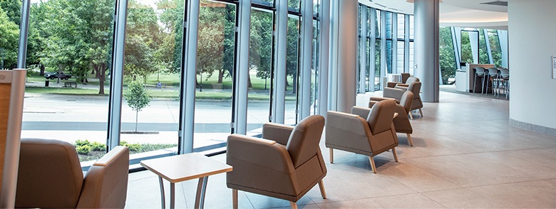 An empty waiting area with a row of comfortable chairs facing towards large windows looking out at many trees