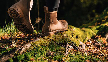 A closeup view of a woman wearing boots and walking on an exposed tree root in a forest.