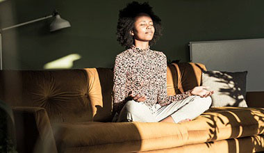 A woman meditating on her couch with the sun in her face.