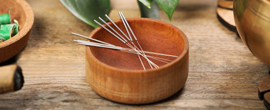 A closeup view of acupuncture needles that are laying in a wooden bowl.