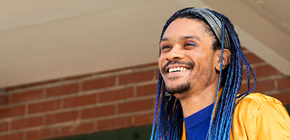 A smiling person with blue braids and colorful eyeshadow 
