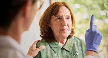 A medical professional wearing a blue glove tests an older woman's eyesight.