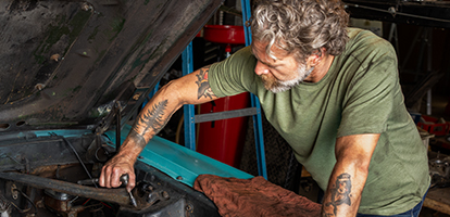 A man leaning into a blue car's hood using a wrench on the engine
