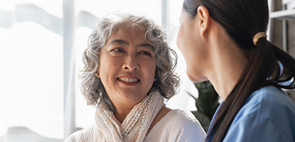 An older woman smiles while talking to a medical professional in blue scrubs.