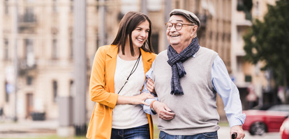 woman smiling as she helps older man with cane walk across the street