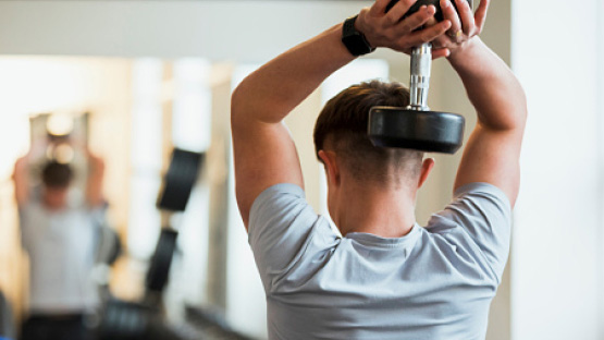 Student athlete lifting a dumbbell behind their head in a weight room.