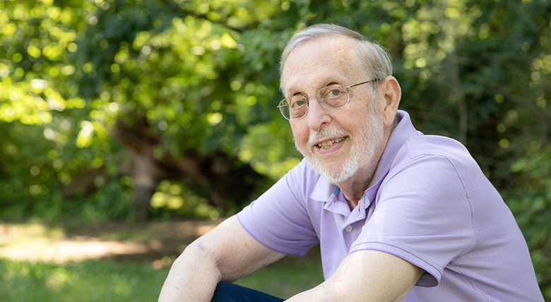 o	AHN patient Carleton Weber smiling while looking into the camera as he is sitting outside on a bench.