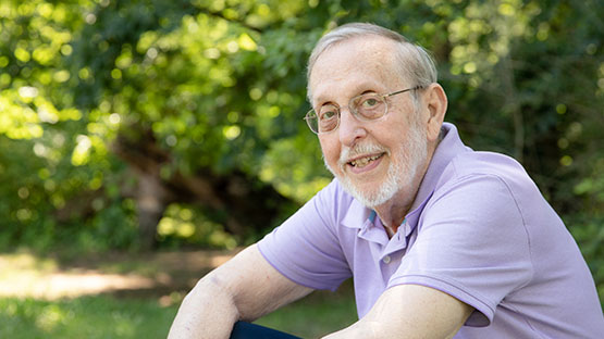 AHN patient Carleton Weber smiling while looking into the camera as he is sitting outside on a bench.