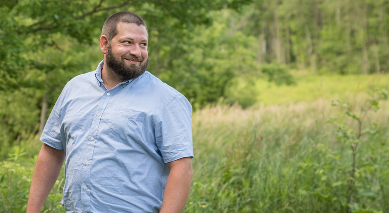 Robert Haupt standing near a field in the woods and smiling and looking off camera.